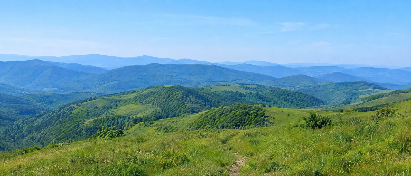 Layered soft green hills receding into blue haze with a meadow footpath in the foreground